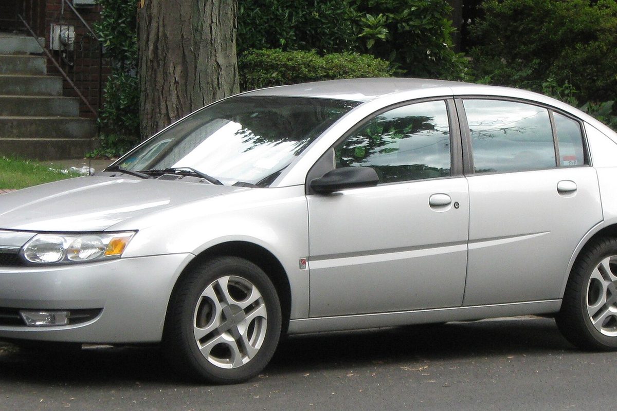 A silver Saturn Ion sedan parked on a driveway in front of a hedge