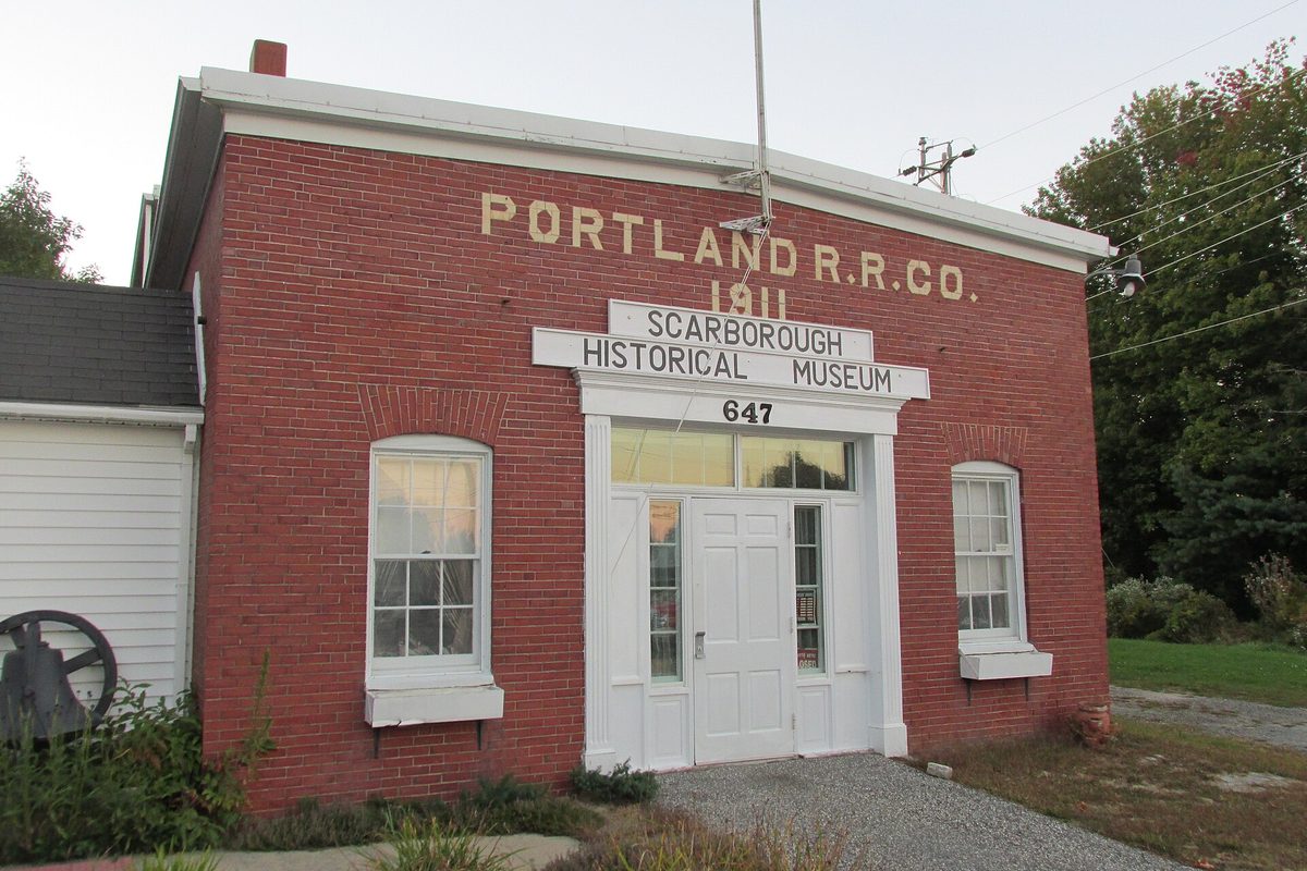 The red brick 1911 Portland Railroad Company building in Scarborough, now the Scarborough Historical Museum, with white double doors, white-trimmed windows and a gravel drive