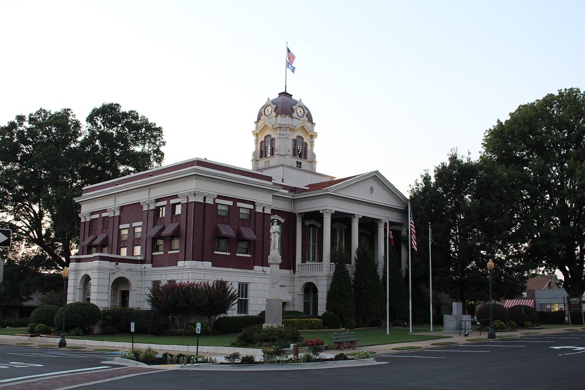 The White County Courthouse in Searcy, a red-brick building with white columns and trim, a domed clock tower and an American flag, seen at dusk