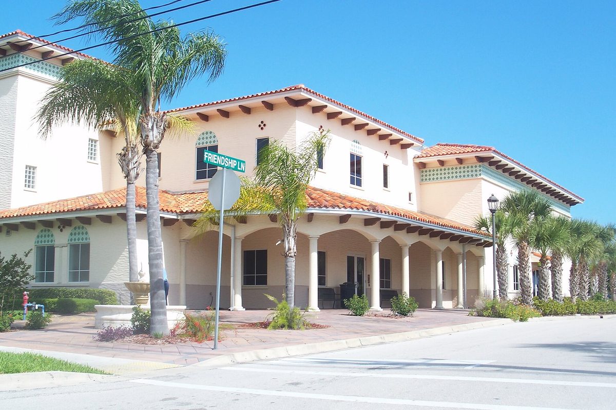 Sebastian City Hall, a cream Spanish-style building with a red tile roof, an arched front porch and palm trees, beside a Friendship Ln street sign