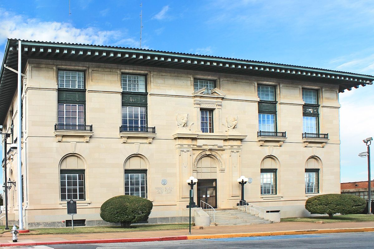 The Sherman U.S. Post Office and Courthouse, a pale stone building with a wide green-trimmed roof overhang, arched ground-floor windows and iron balconies, under a blue sky