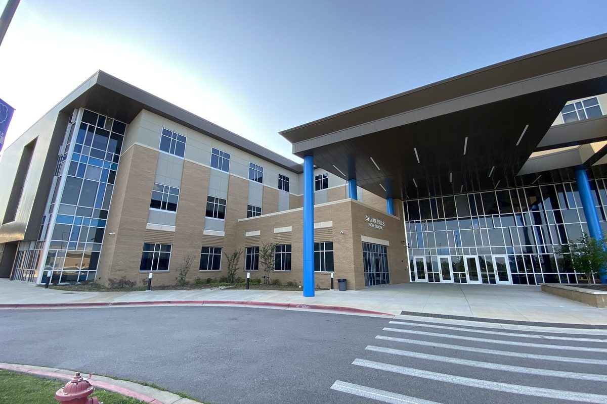 The front entrance of Sylvan Hills High School in Sherwood, a modern brick and glass building with blue columns holding up a wide canopy