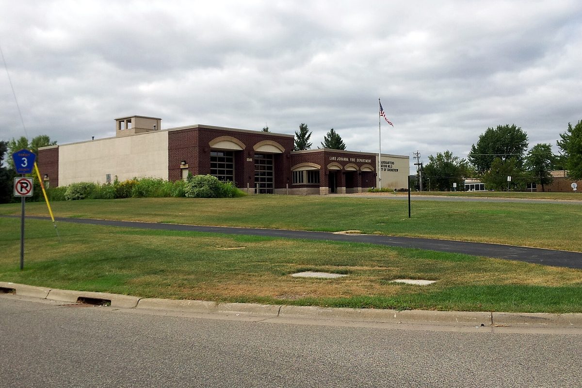 The brick Lake Johanna Fire Department station in Shoreview, with a flagpole, a wide lawn and road signs by the curb