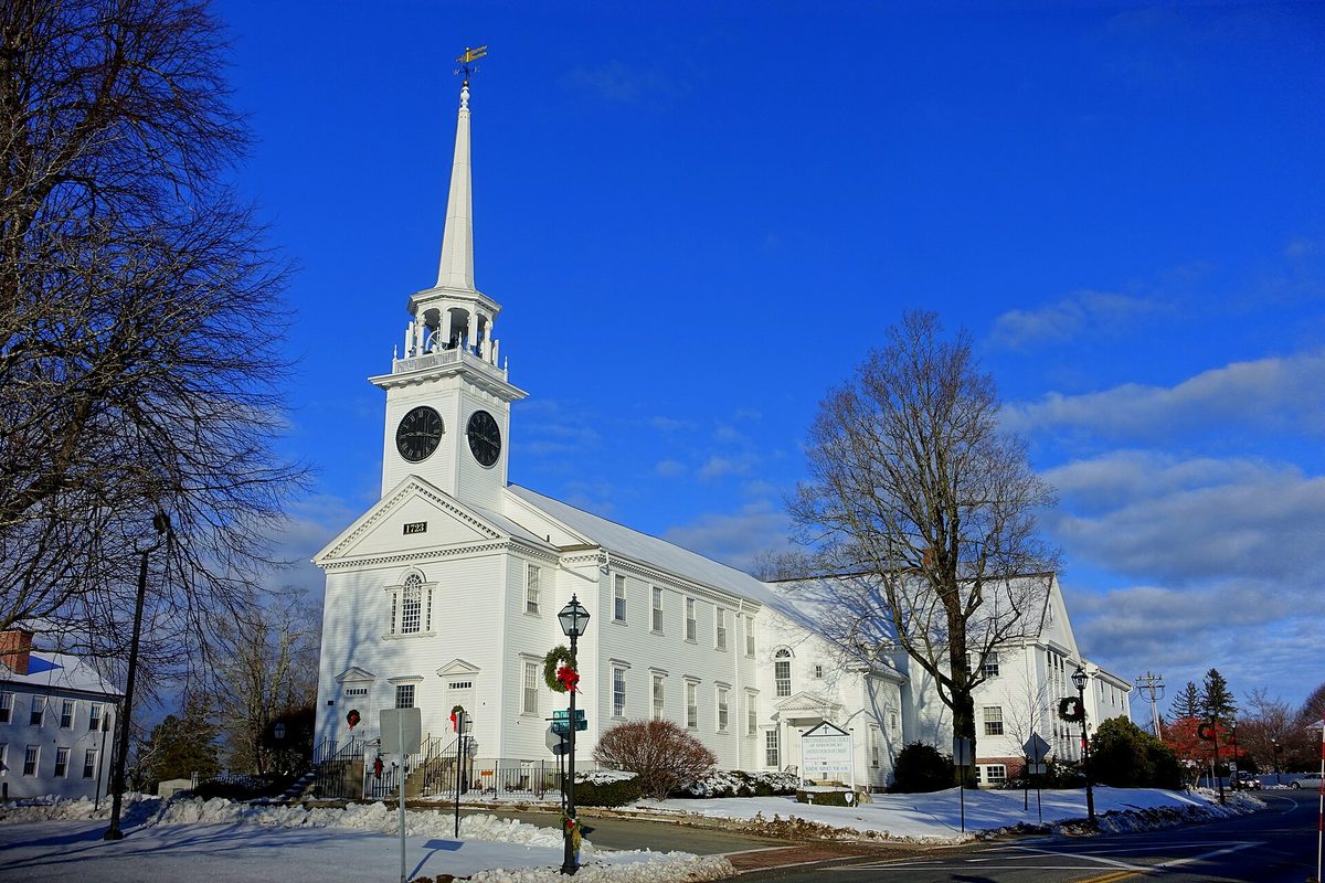 Shrewsbury's white First Congregational Church with a tall steeple and twin clock faces, snow on the lawn under a bright blue sky