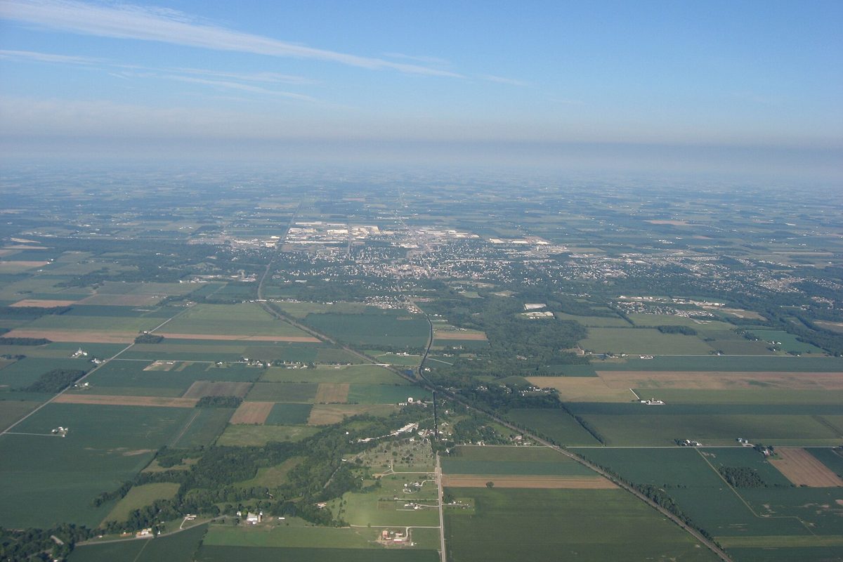 Aerial view of Sidney from the east, with square farm fields and tree lines in front and the city spread out in the hazy distance
