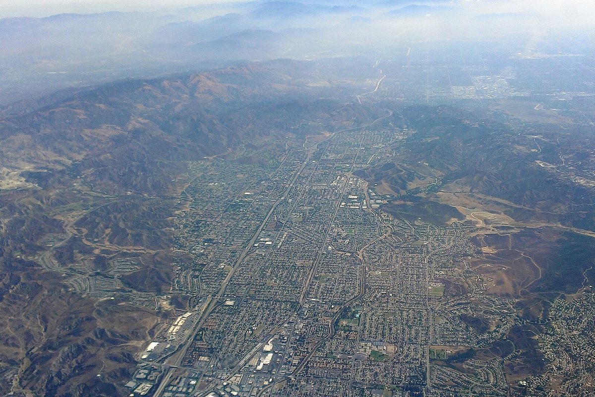 Aerial view of Simi Valley, a dense grid of streets and homes filling the valley floor between brown mountain ridges under a hazy sky