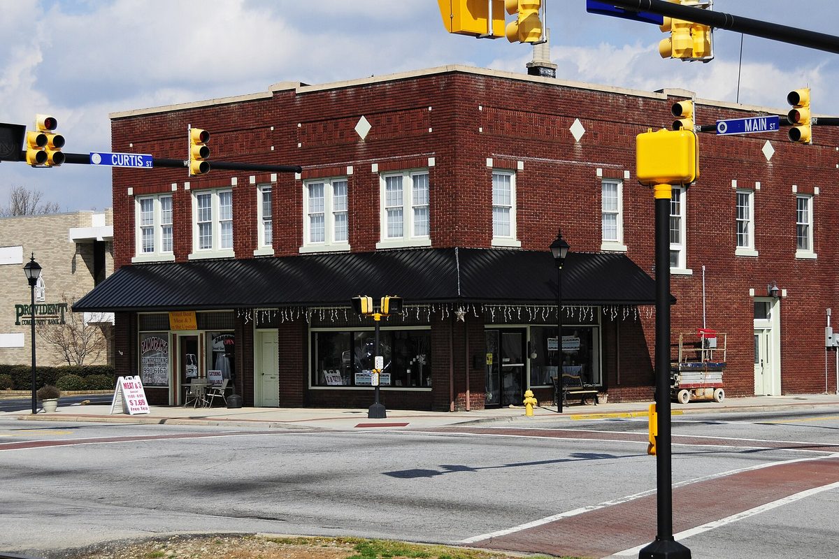 A two-story red brick corner building at Main and Curtis streets in Simpsonville, with yellow traffic signals and a black awning