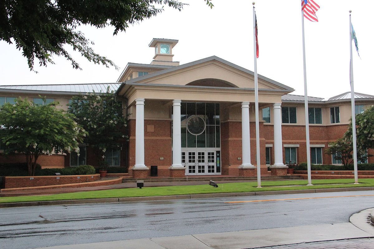 Smyrna City Hall, a red brick building with a white-columned entrance, a small clock tower and three flags on poles, seen from a wet street