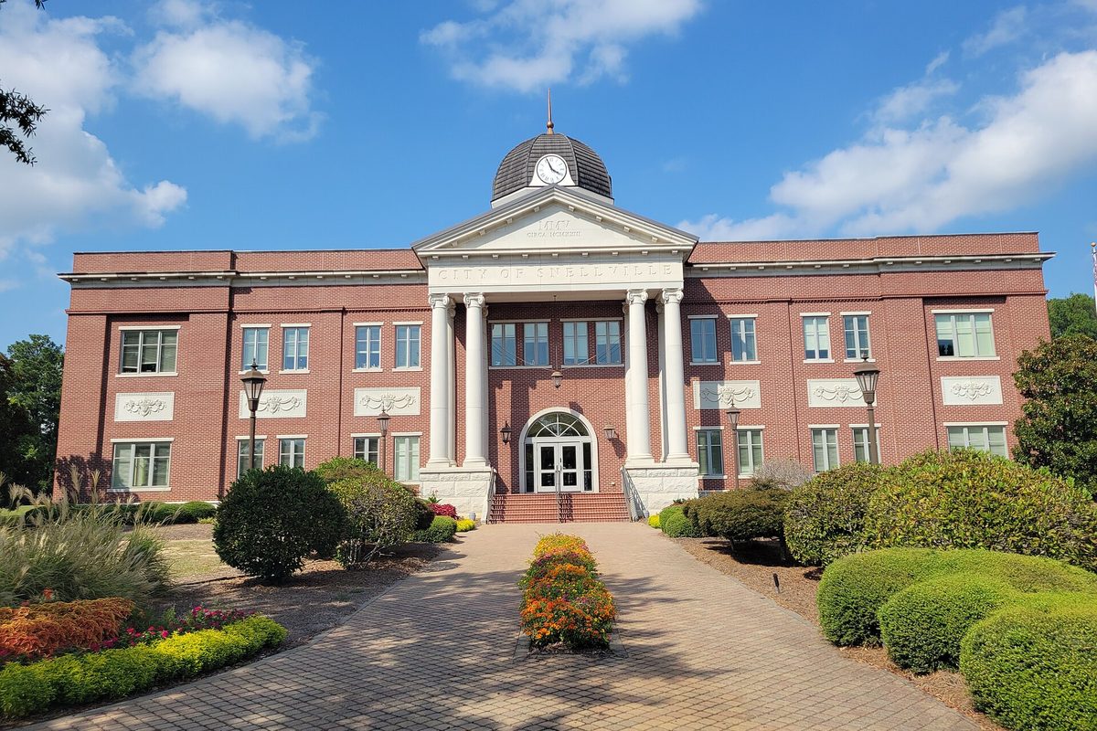 Snellville City Hall, a red-brick building with a white columned portico and a clock dome, behind a brick walk and flower beds