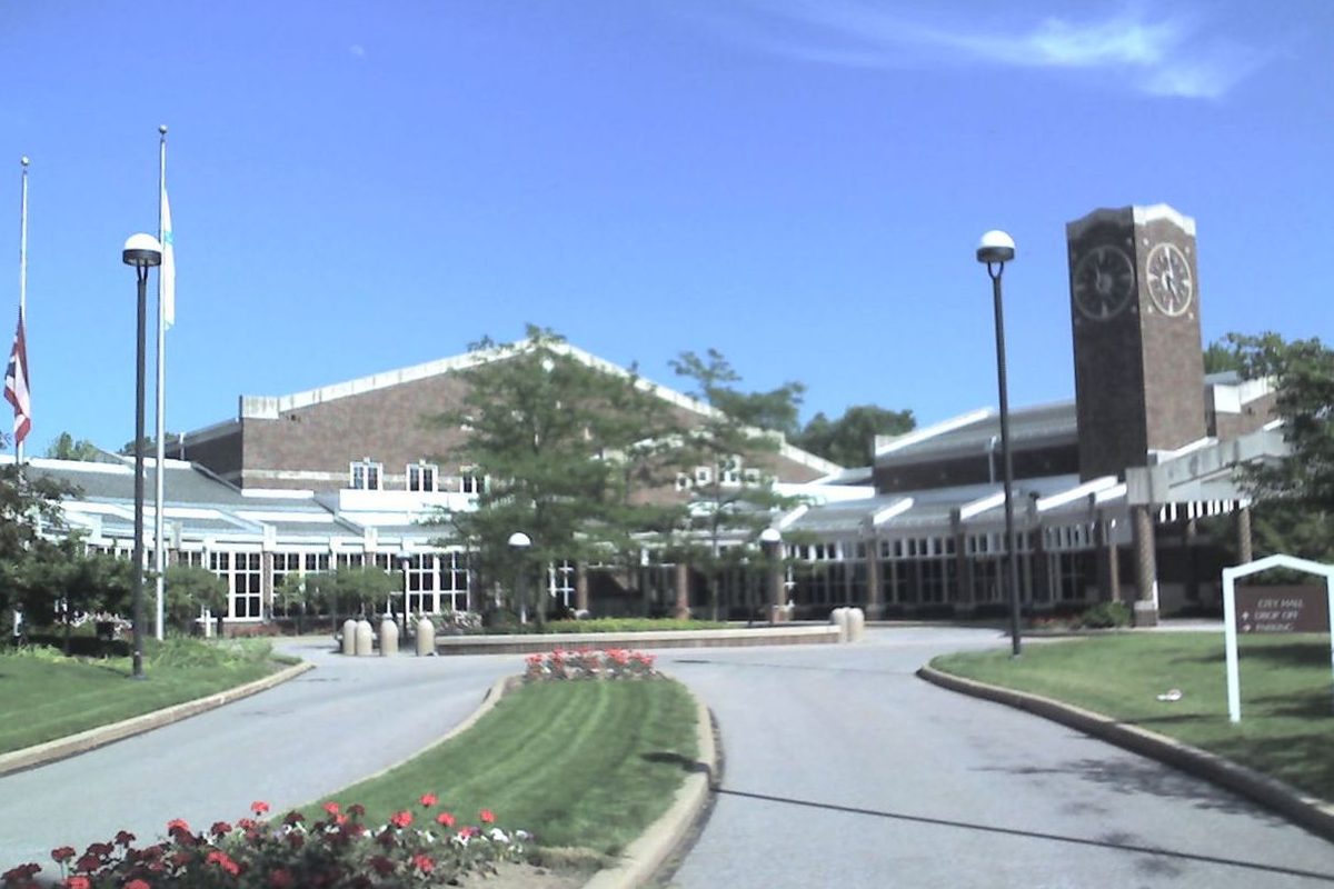 Solon City Hall, low brick buildings with a brick clock tower, flagpoles and a curving drive edged with red flowers under a clear blue sky