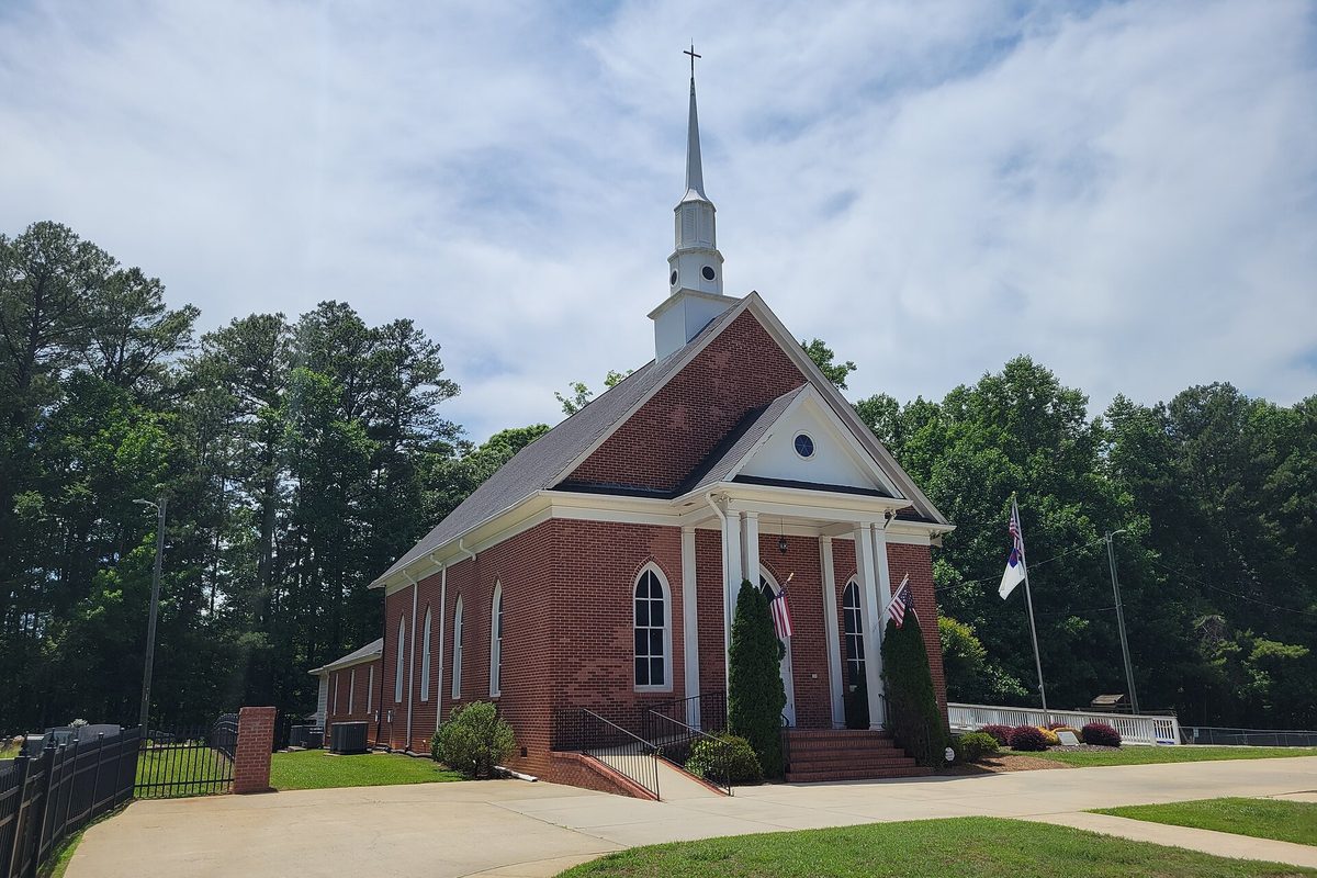 Mount Vernon Baptist Church in South Fulton, a red brick church with white columns and a tall white steeple, flags out front and tall pines behind