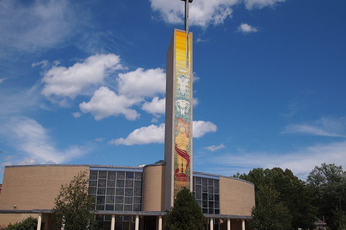 Holy Cross Church in South Portland, a rounded tan building with tall windows and a tall mosaic tower showing religious figures, against a blue sky