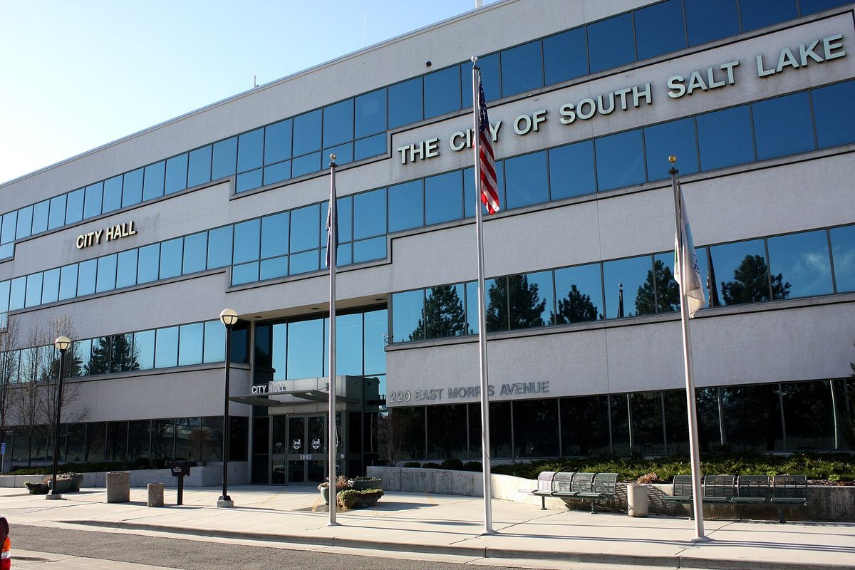 South Salt Lake City Hall, a pale four-story building with long bands of blue glass and flags out front, at 220 East Morris Avenue