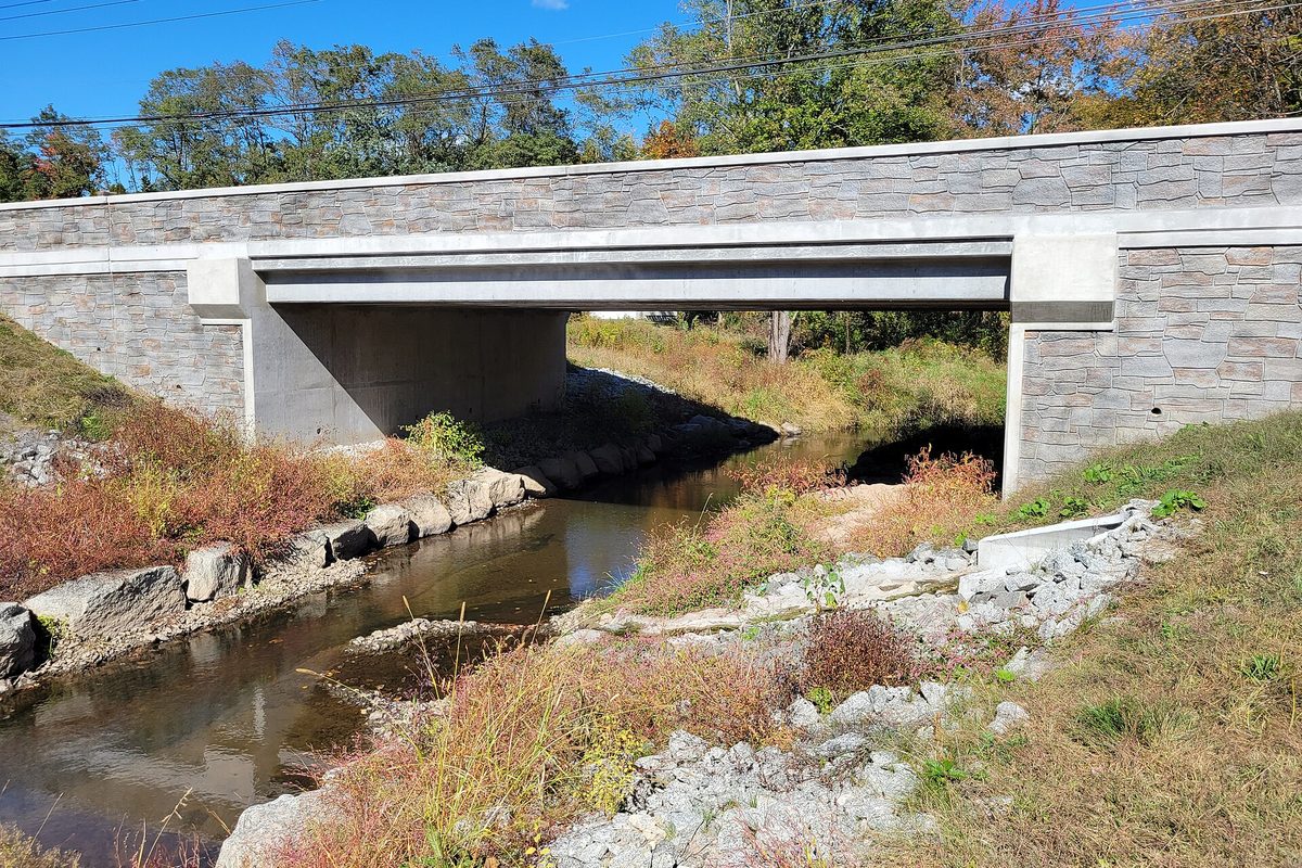 A stone-faced road bridge carrying Pleasant Valley Road over the shallow Podunk River in South Windsor on a sunny autumn day