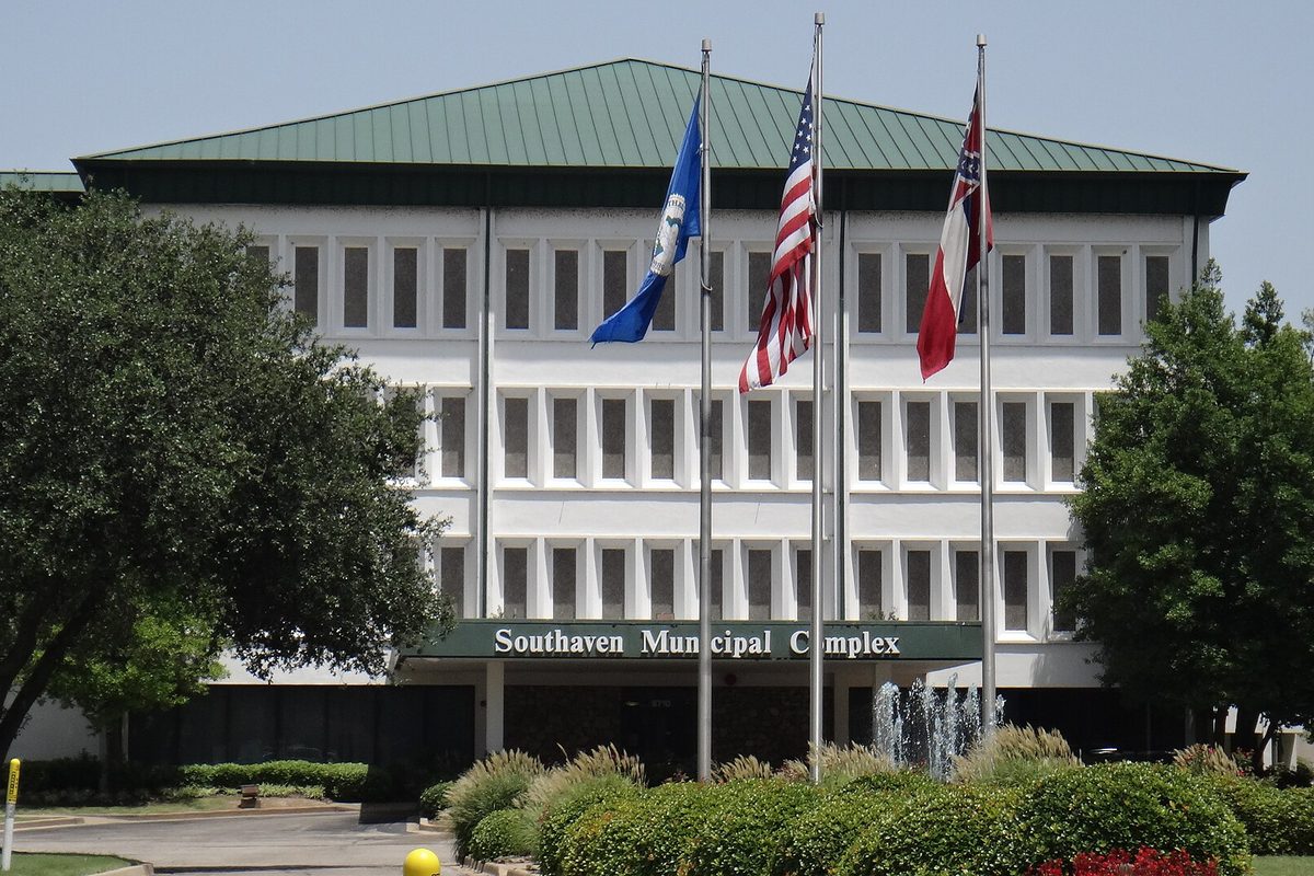 The Southaven Municipal Complex, a white building with a green roof, three flags and a fountain in front