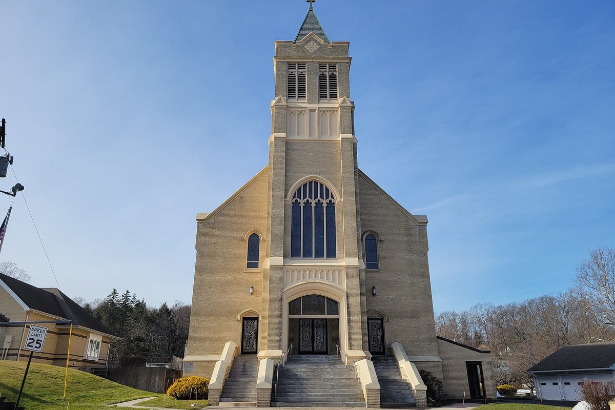 Immaculate Conception Church in Southington, a tan brick church with a tall square bell tower, an arched stained-glass window and wide stone steps under a clear blue sky