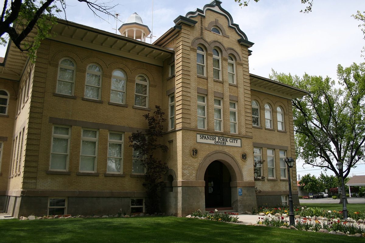 Spanish Fork City Offices, a yellow-brick former schoolhouse with tall arched windows, a cupola and flower beds along the entrance walk