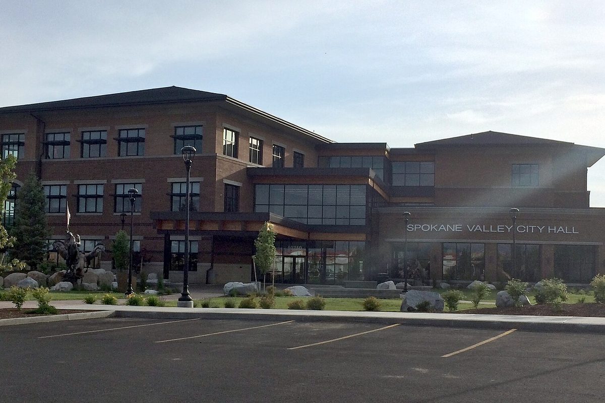 The three-story brick Spokane Valley City Hall with its name on the front and an empty parking lot in the foreground
