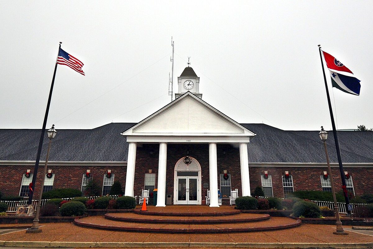 Spring Hill City Hall, a brick building with a white columned portico and a clock cupola, between an American flag and a Tennessee flag on an overcast day