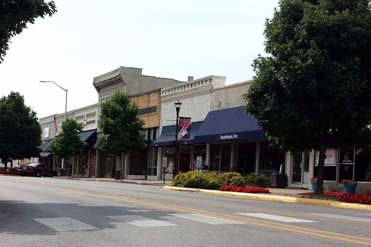 Old brick storefronts with blue awnings along East Emma Avenue in downtown Springdale, with trees, a street lamp and a crosswalk