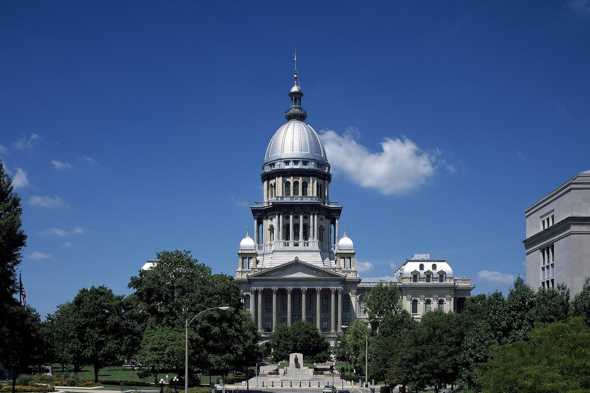 The domed Illinois State Capitol in Springfield rising above green trees under a deep blue sky with one white cloud