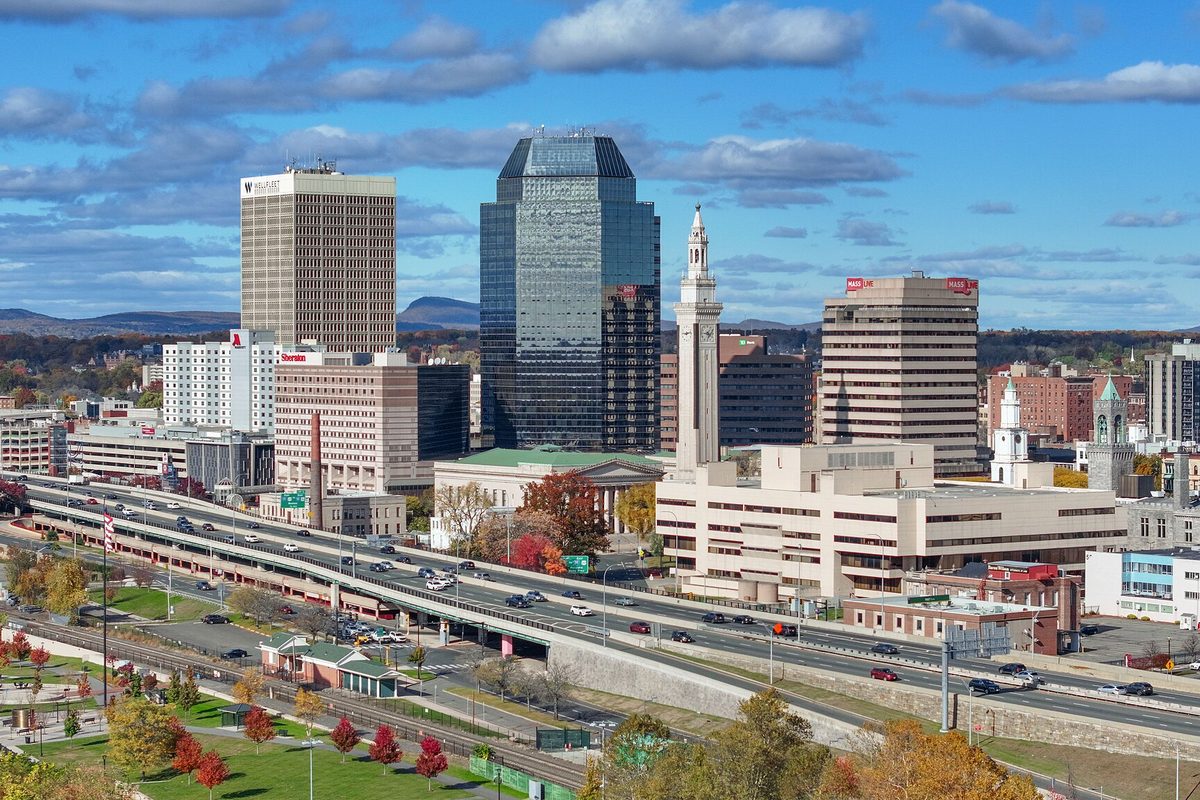 Downtown Springfield on a clear autumn day: office towers and a white clock tower behind an elevated highway that curves past a park with red trees