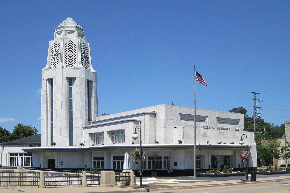 The white Art Deco St. Charles Municipal Center with its tall carved tower and a flagpole out front, under a clear blue sky