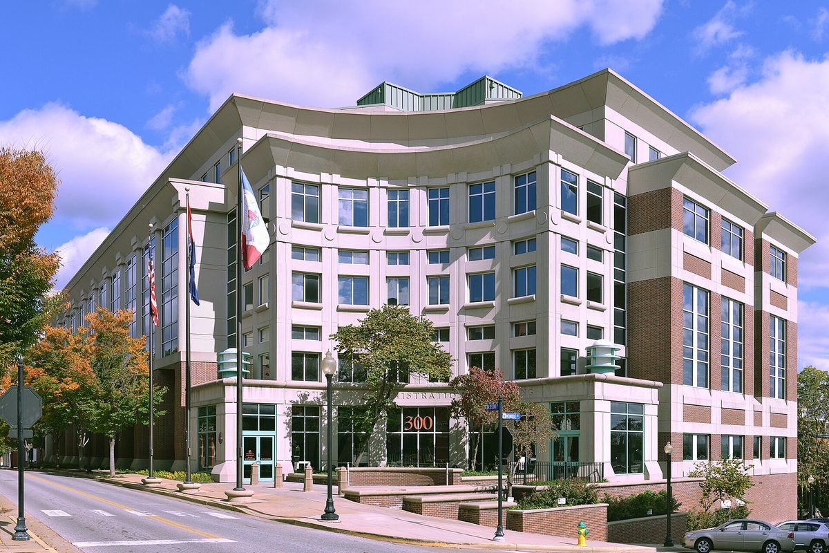 The St. Charles County Courthouse, a curved multi-story building with flags out front and autumn trees along the street, under a blue sky
