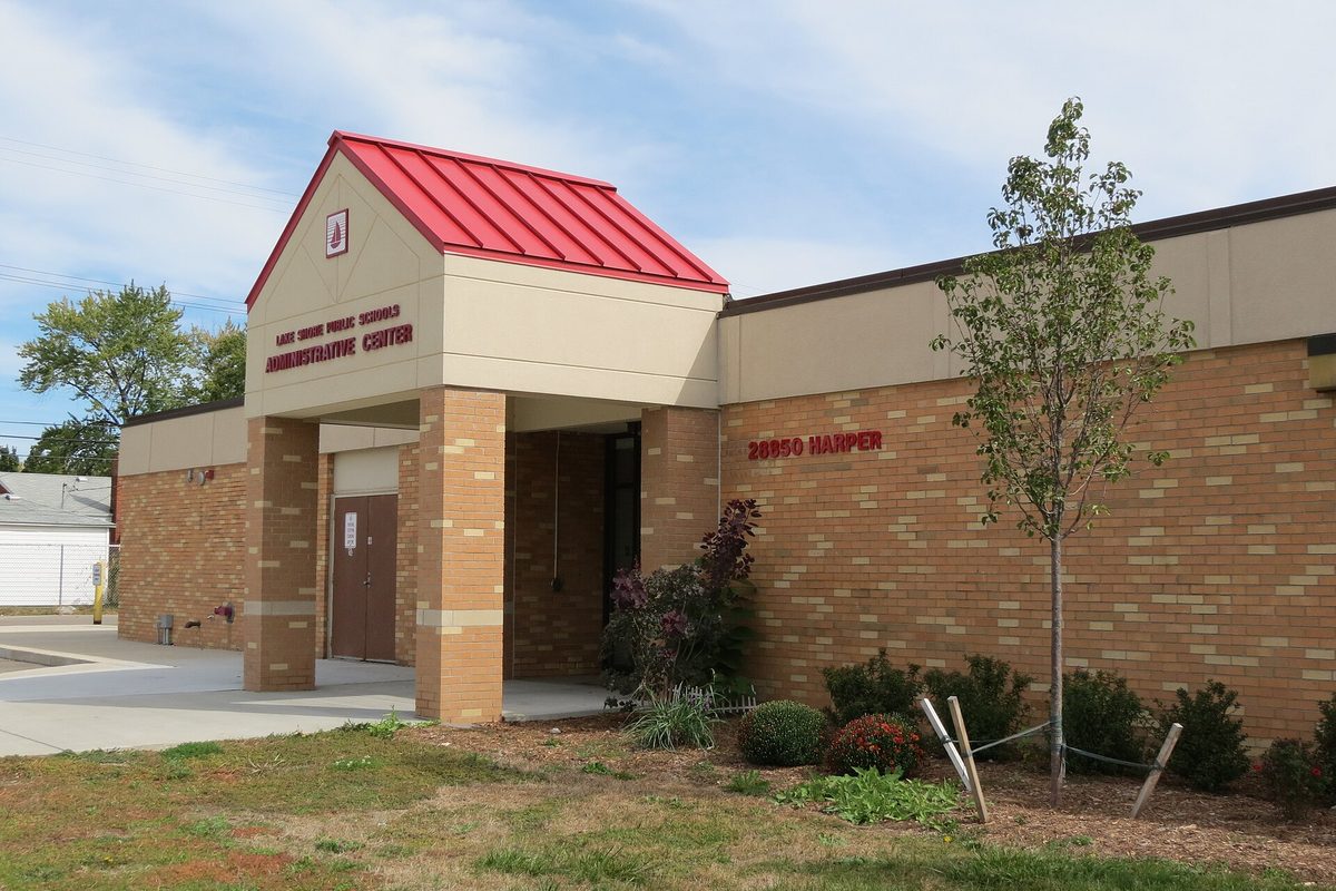 The tan brick Lake Shore Public Schools Administrative Center at 28850 Harper, with a red metal roof over the entrance and a young tree out front