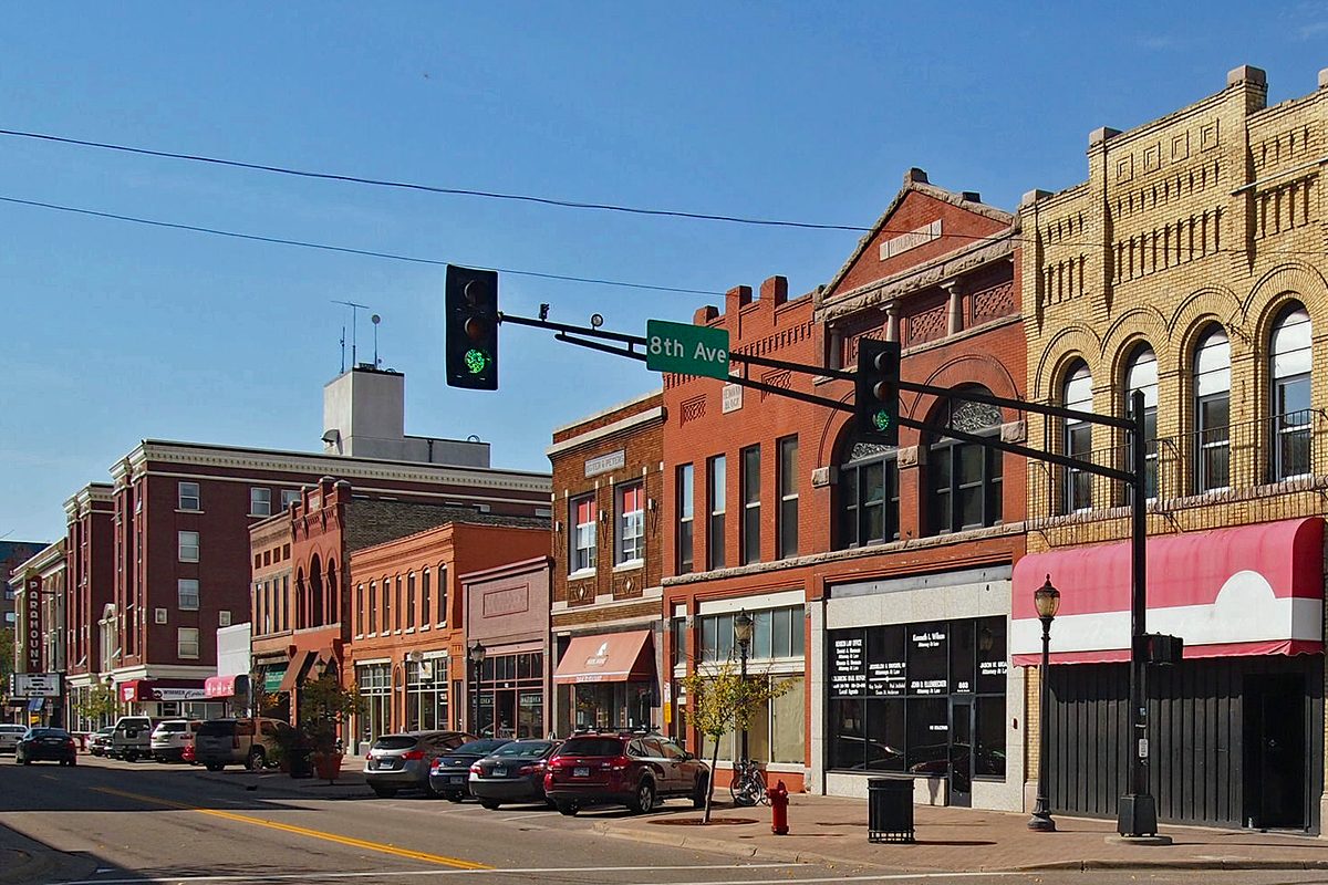 Brick and stone storefronts on the 800 block of St. Germain Street in downtown St. Cloud, with an 8th Ave street sign and a green traffic light under a clear blue sky