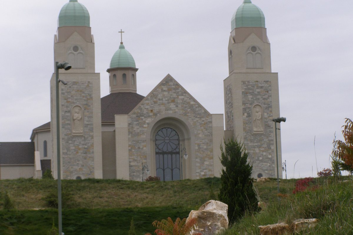 St. John the Evangelist church in St. John, a stone church with two green-domed towers and a central cupola with a cross, on a grassy hill