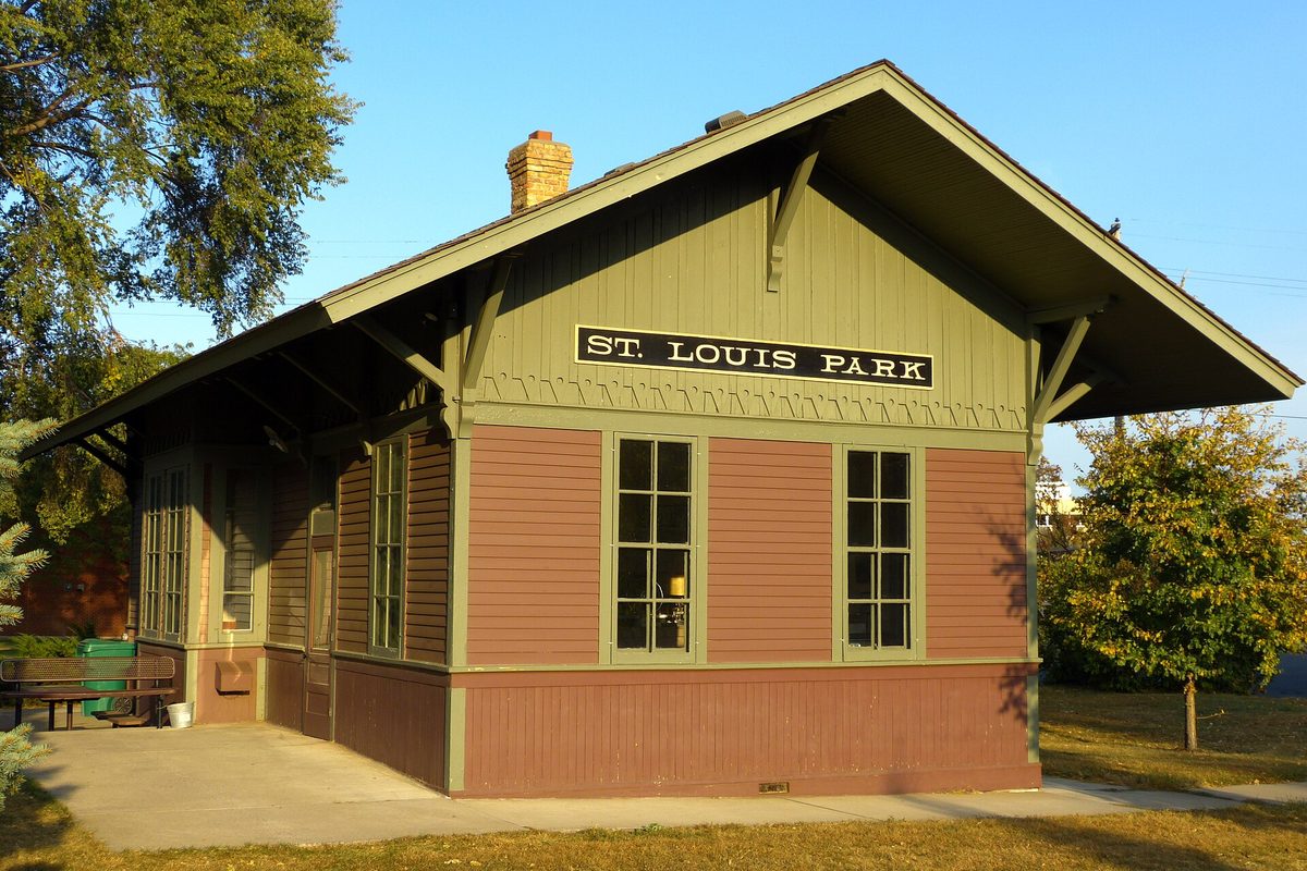 The restored red and green Milwaukee Road depot in St. Louis Park, with a St. Louis Park sign under its wide gable roof, lit by late-afternoon sun