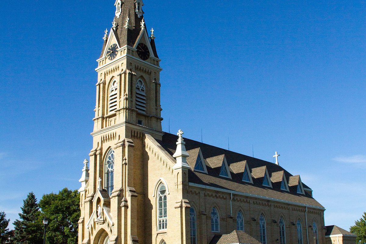 The tall cream-brick Church of St. Michael with its clock tower, spire and row of dormers against a deep blue sky