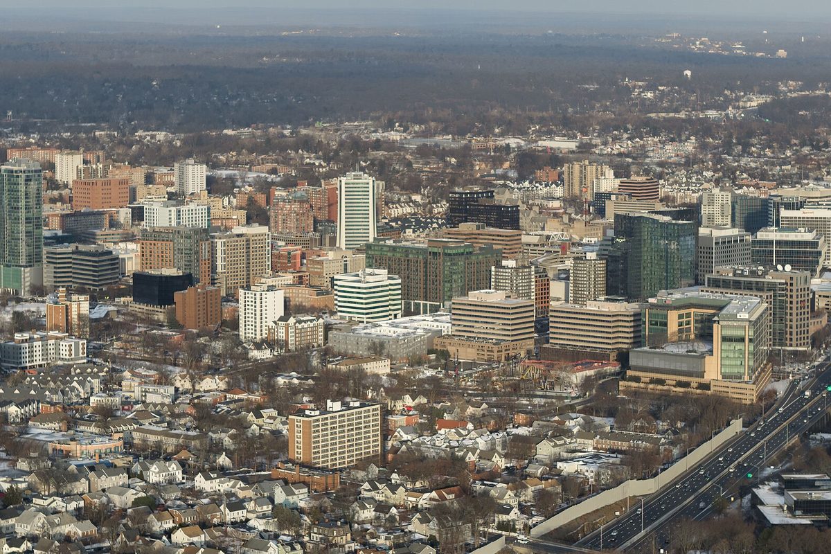 Aerial view of downtown Stamford in winter, with glass office towers rising over snow-dusted houses and Interstate 95 curving along the right edge