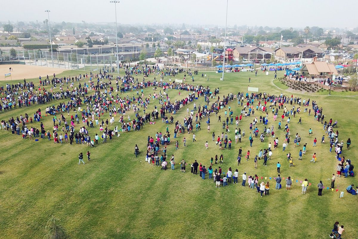 Aerial view of a large crowd spread across the grass of a Stanton park for an Easter egg hunt, with houses and ball fields behind