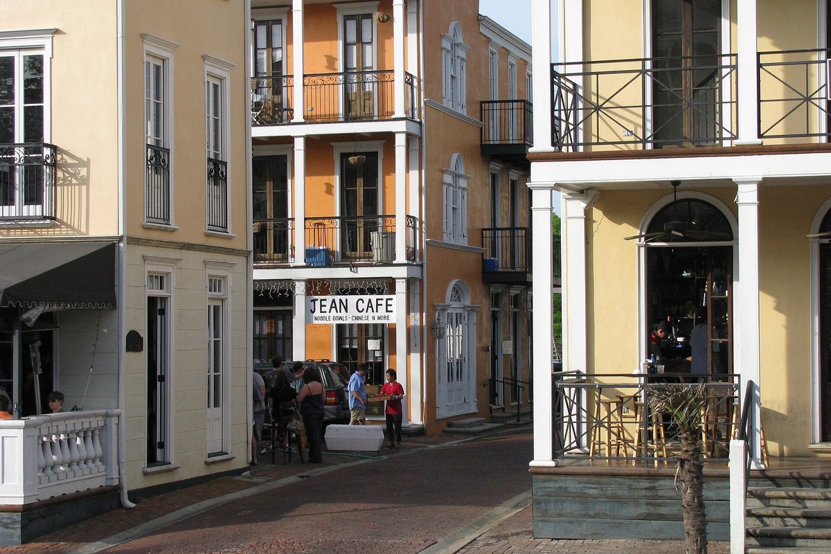 Pastel buildings with iron balconies and a Jean Cafe sign along a brick street in Starkville's Cotton District