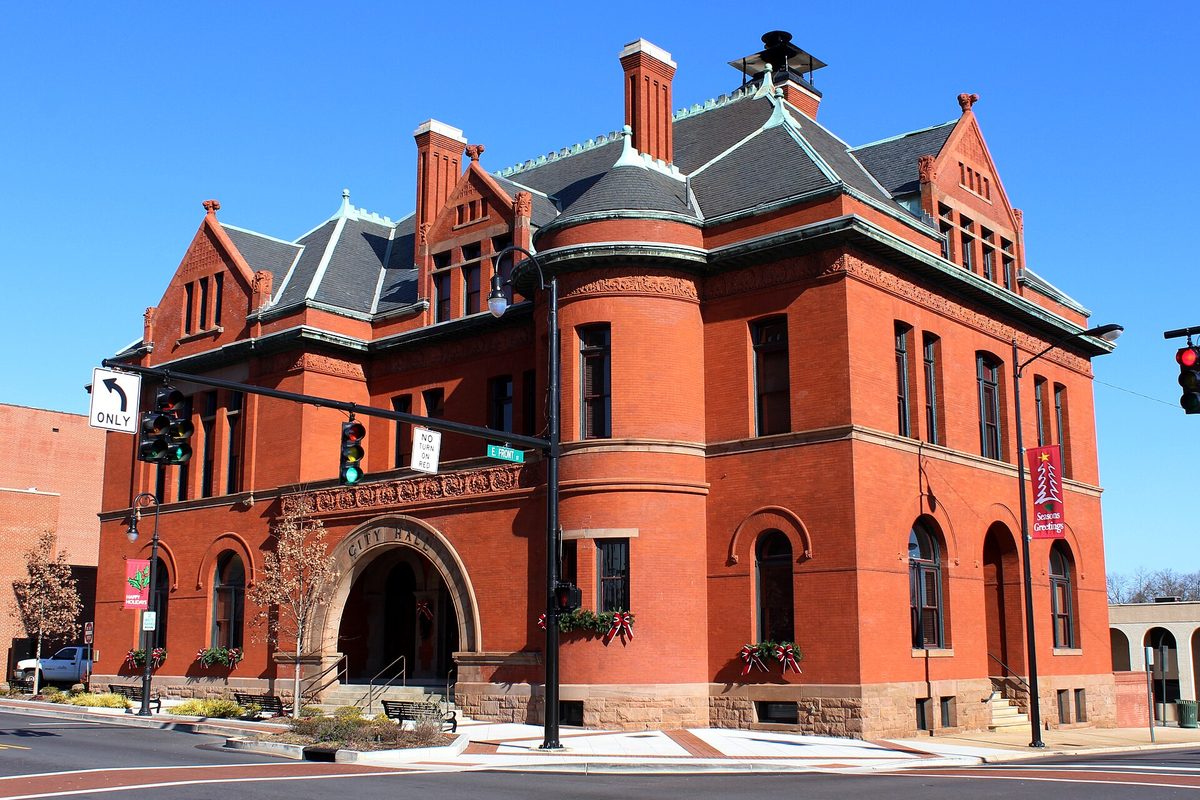 Statesville's red brick City Hall from the early 1890s, with a round corner tower, a slate roof and an arched entrance, at a downtown intersection