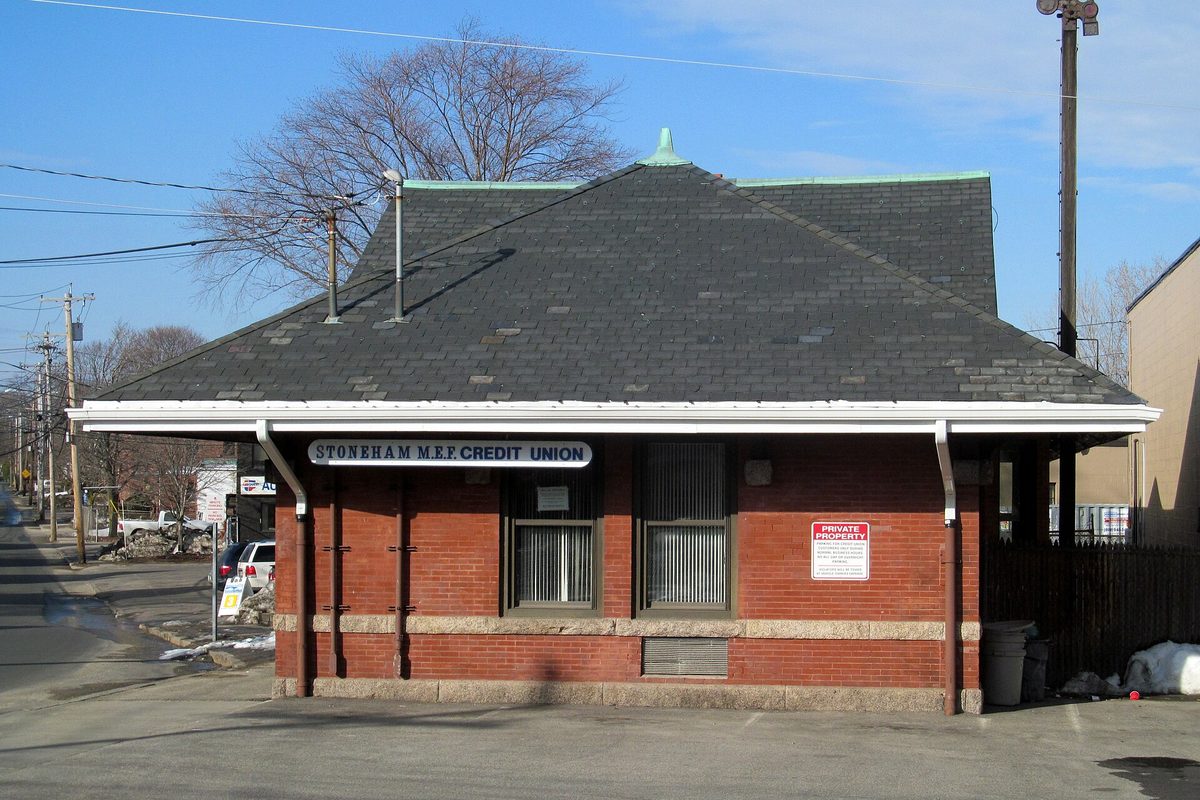 The former Stoneham railroad station, a small red-brick building with a slate hip roof and white trim, now used as a credit union branch