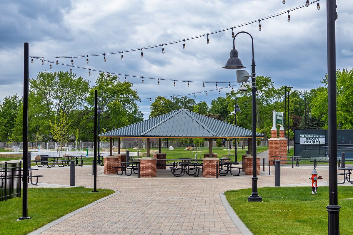 Strongsville Town Center Park on a cloudy day, with a picnic pavilion on brick pillars, strings of lights overhead and a sign for the sport courts
