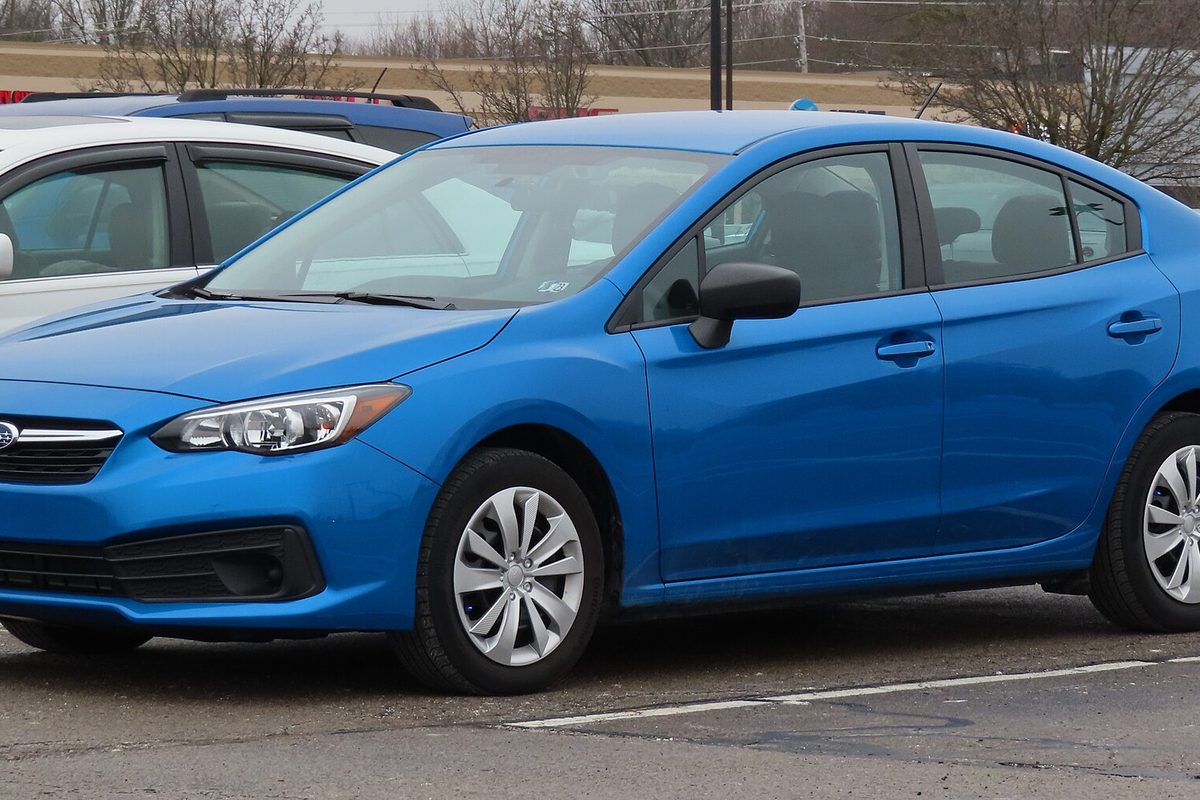 A bright blue 2021 Subaru Impreza sedan in a parking lot on a gray winter day