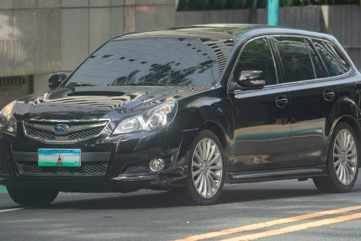 A black 2012 Subaru Legacy wagon on a city street in front of a gray wall