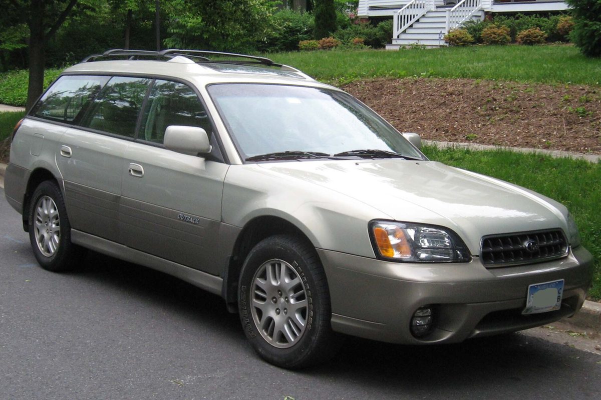 A champagne-colored early-2000s Subaru Outback wagon parked at a curb beside a lawn