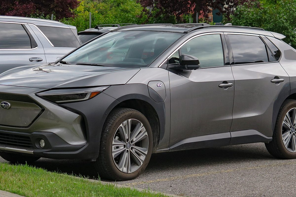 A gray Subaru Solterra electric SUV with black wheel arches and silver wheels, parked on a lot beside a strip of grass