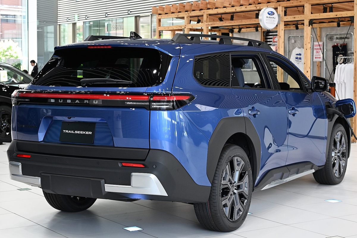 Rear view of a blue Subaru Trailseeker electric SUV with roof rails and black wheel arches on a showroom floor