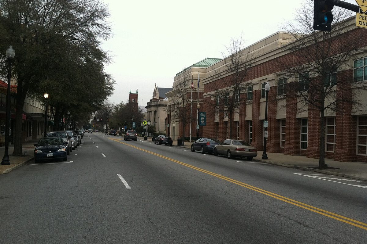 North Main Street in downtown Suffolk on an overcast day, with cars parked along both curbs, bare trees and red brick buildings lining the sidewalk