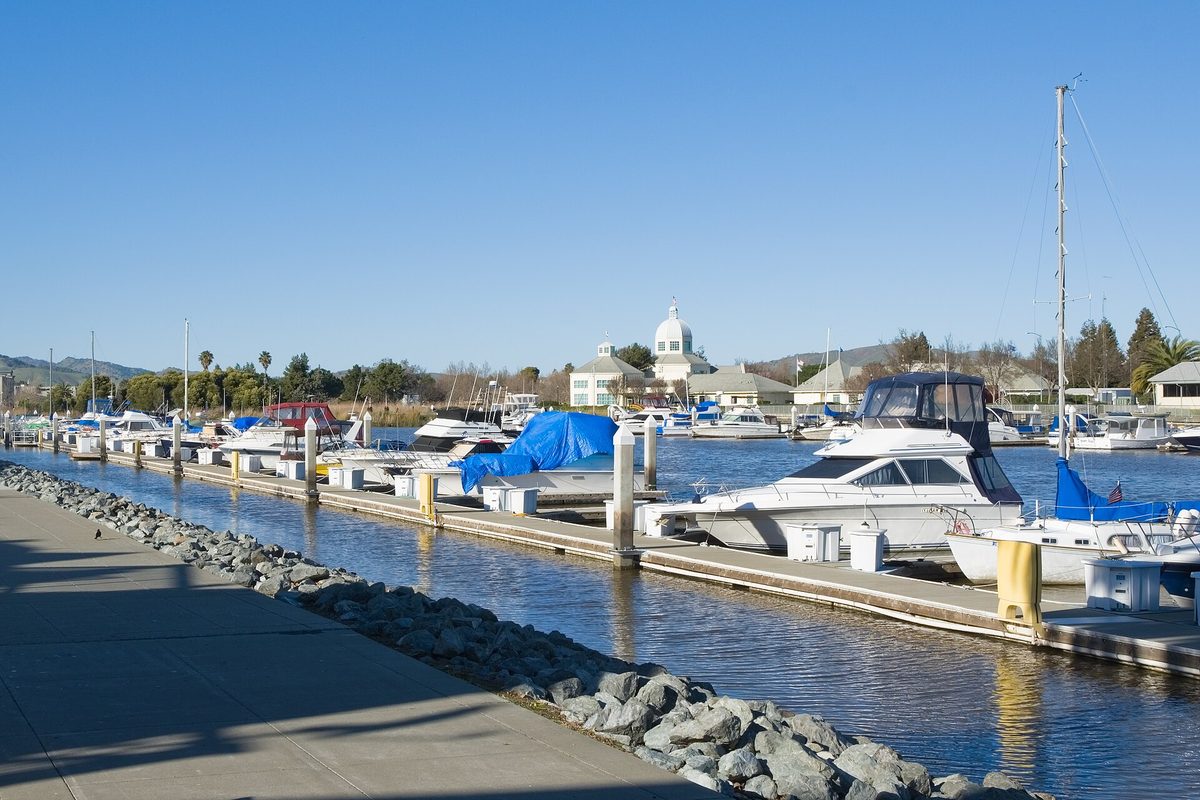 Motorboats and sailboats tied up at the Suisun City Marina, with the white domed City Hall across the water under a clear blue sky