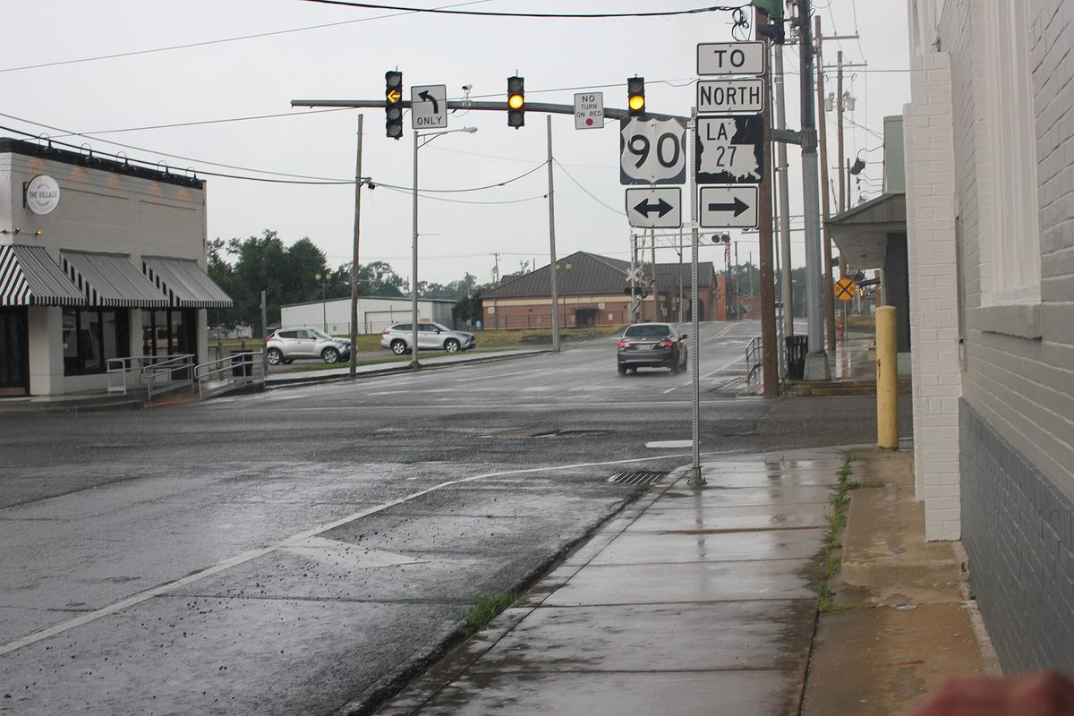A rainy downtown Sulphur intersection with traffic lights and signs pointing to U.S. 90 and LA 27
