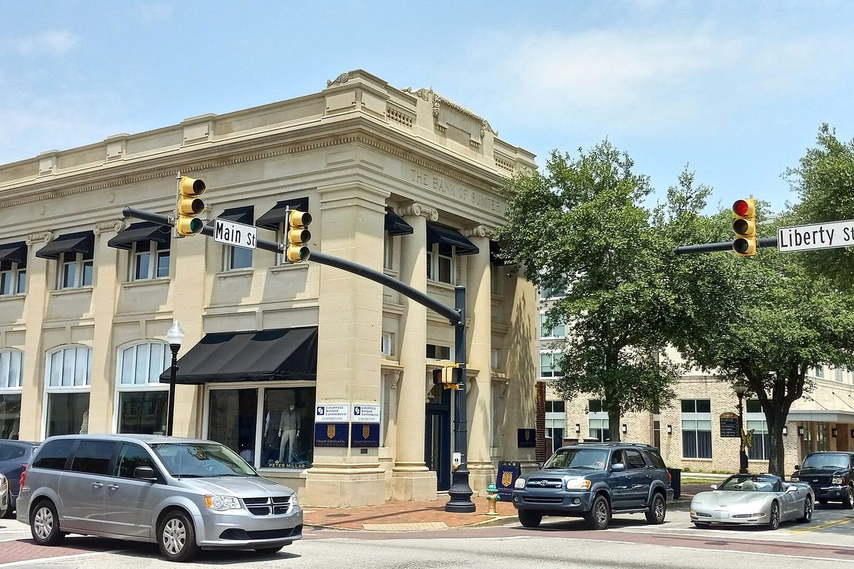 The cream stone Bank of Sumter building on the corner of Main and Liberty streets, with traffic lights, a silver minivan and an SUV at the intersection