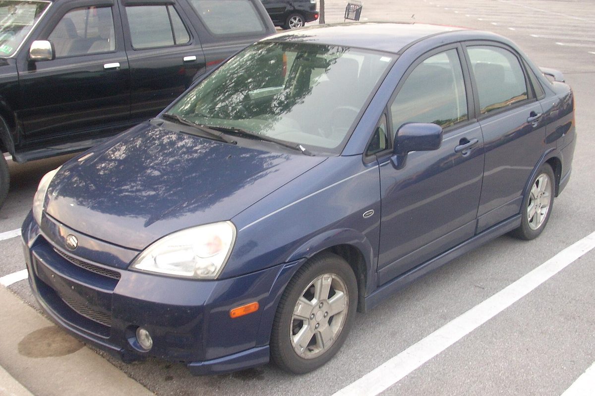 A dark blue Suzuki Aerio sedan with alloy wheels and a scuffed front bumper, parked in a parking lot