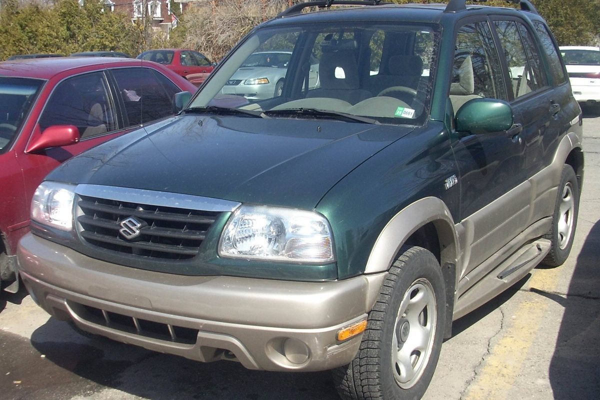 A dark green four-door Suzuki Grand Vitara with tan lower trim and roof rails, parked on a city street